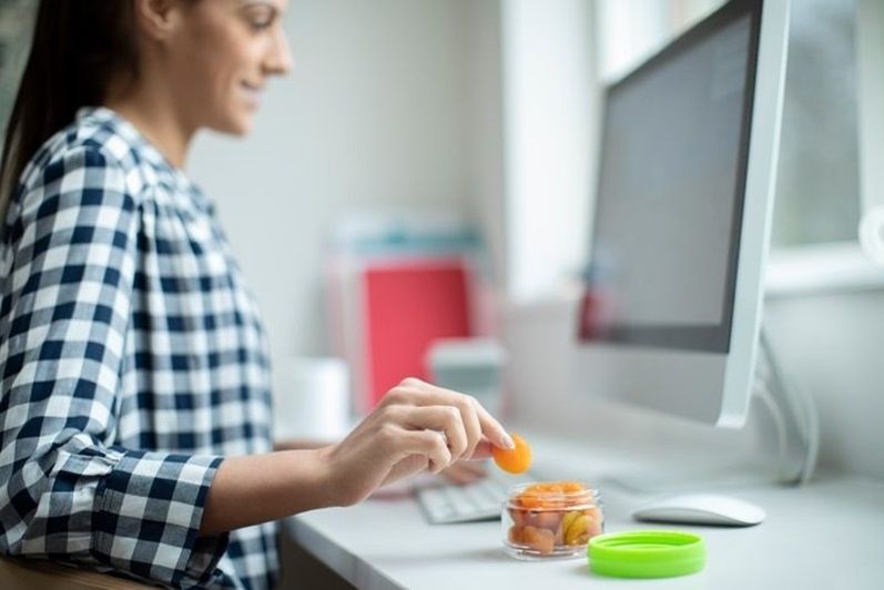 Femme prenant une bouchée de fruit à son bureau devant un ordinateur