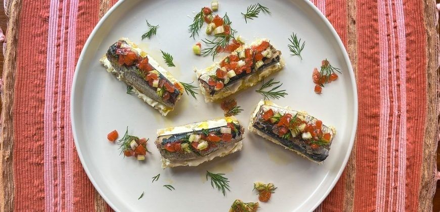 Quatre tartines garnies de sardines, tomates et aneth sur une assiette